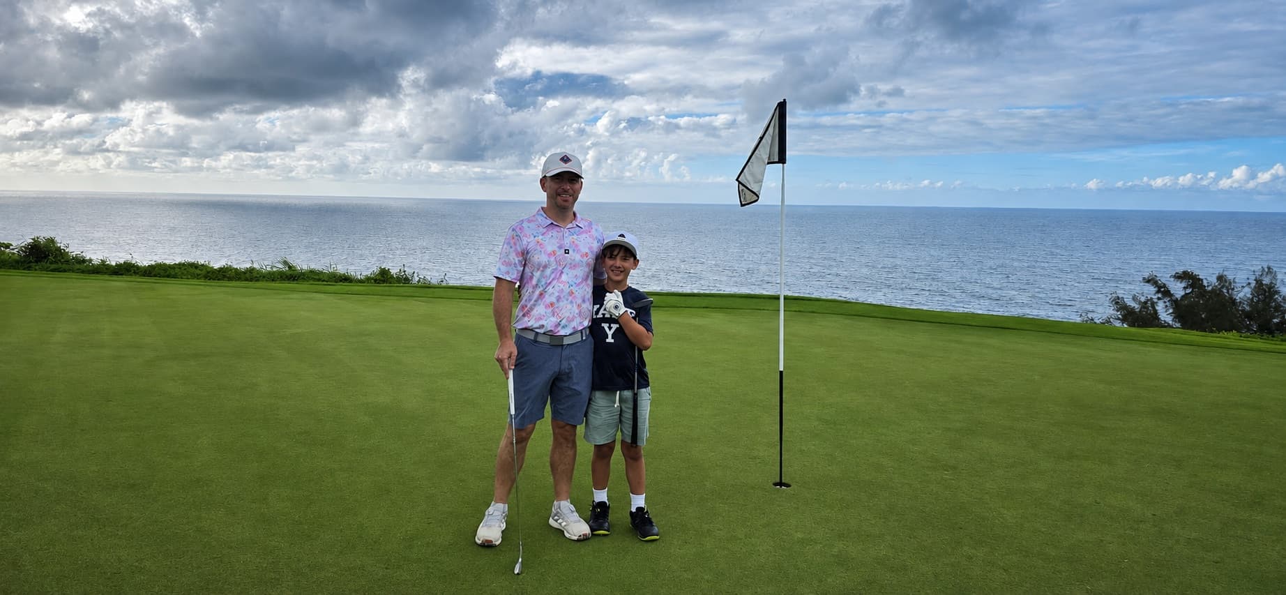 A father and his son standing together on a putting green beside the ocean